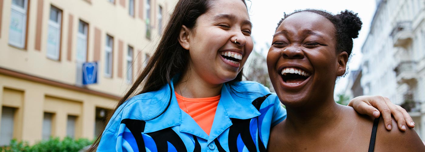 Two women laughing together in a vibrant city setting, enjoying each other's company and the urban atmosphere.