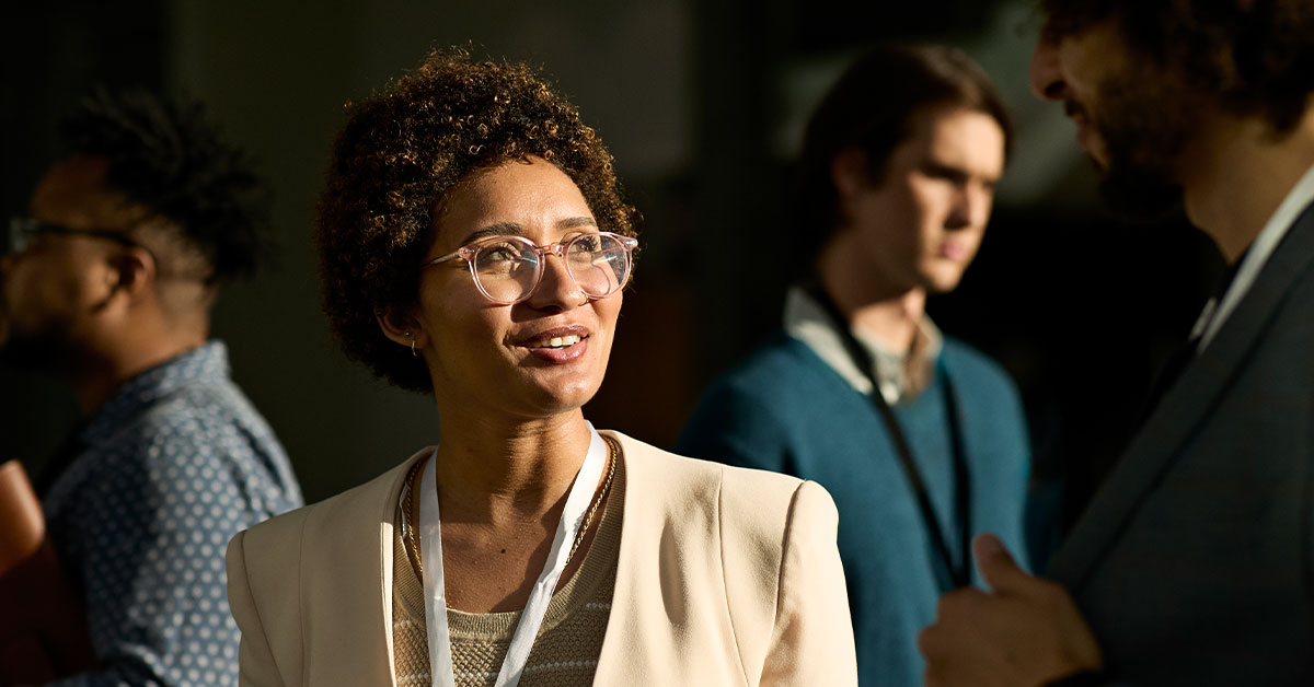 A woman with glasses engaged in conversation with a group of people around her.