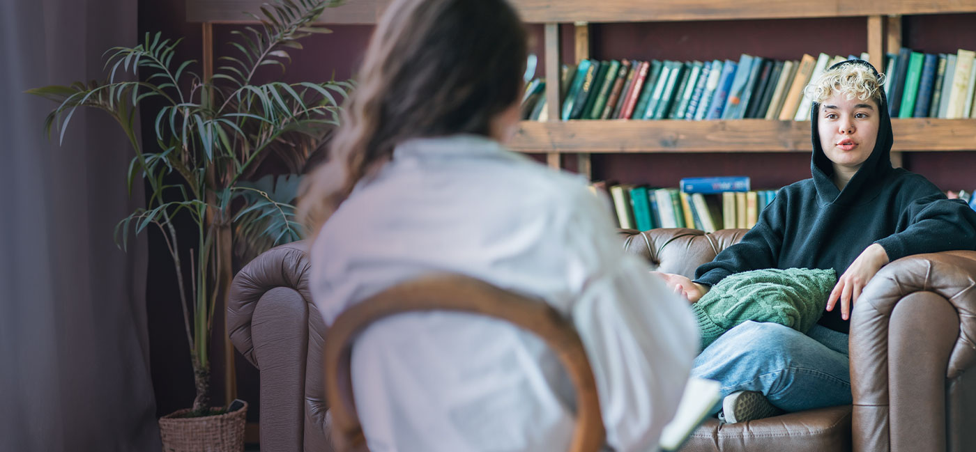 A woman sitting on a couch, reading a book placed on a table in front of her.