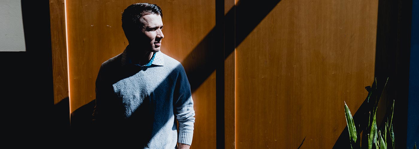 A man stands in front of a door, casting a shadow on the ground beside him.