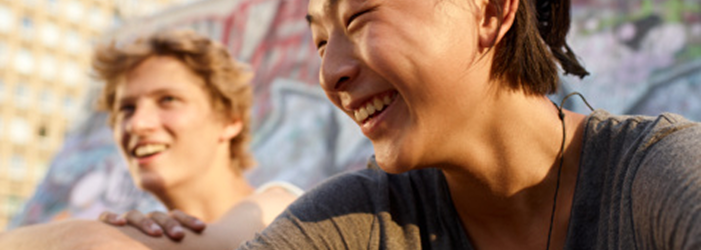 Two young people smiling and laughing in front of a colorful graffiti wall.