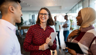 Three diverse colleagues laugh and connect in an office hallway, representing what social workers do day to day