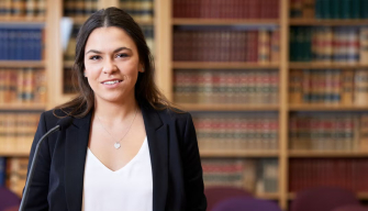 A smiling law student holds a book outside, representing the journey of becoming a lawyer in Australia.
