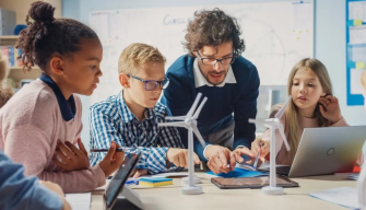 A teacher and students gather around wind turbines in a classroom, illustrating why STEM is important in education careers