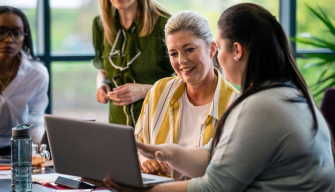 Education professionals collaborate around a laptop, representing career opportunities with a Master of Education