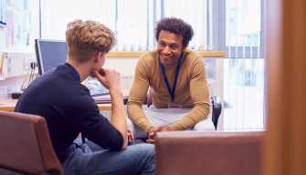 A school counsellor leans forward attentively during a one-on-one session with a young male client