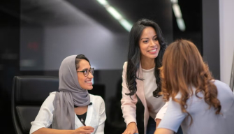 Three women professionals engage in a discussion around a table, representing what public policy is and how it works