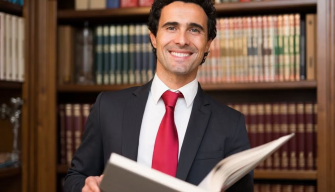 A lawyer in a suit smiles in front of a bookshelf full of law books, representing reasons to study law