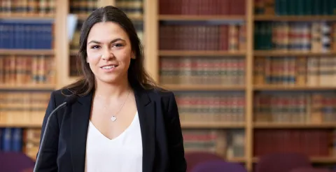 A smiling law student holds a book outside, representing the journey of becoming a lawyer in Australia.