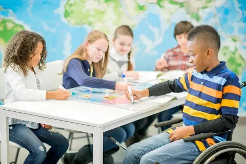 A diverse group of children and a teacher engage in inclusive early childhood education activities in a classroom.