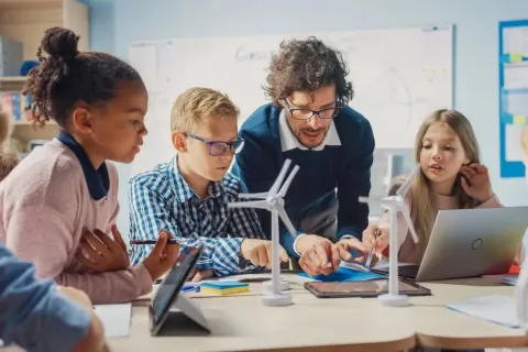 A teacher and students gather around wind turbines in a classroom, illustrating why STEM is important in education careers