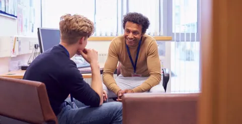 A school counsellor leans forward attentively during a one-on-one session with a young male client