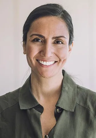A smiling woman stands in front of a classroom, engaging with students and creating a positive learning environment.