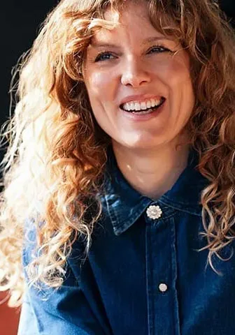 A woman smiling while seated at a table, exuding warmth and positivity.