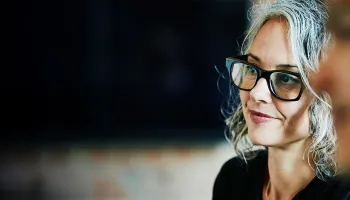 1. A woman and a man, both wearing glasses, are smiling and engaged in conversation.