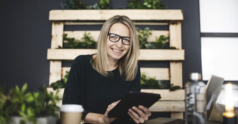 A smiling professional woman holds a tablet in a modern workspace, representing top productivity apps for working students