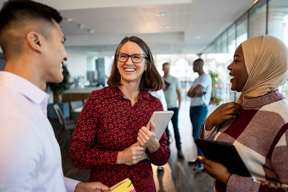 Three diverse colleagues laugh and connect in an office hallway, representing what social workers do day to day