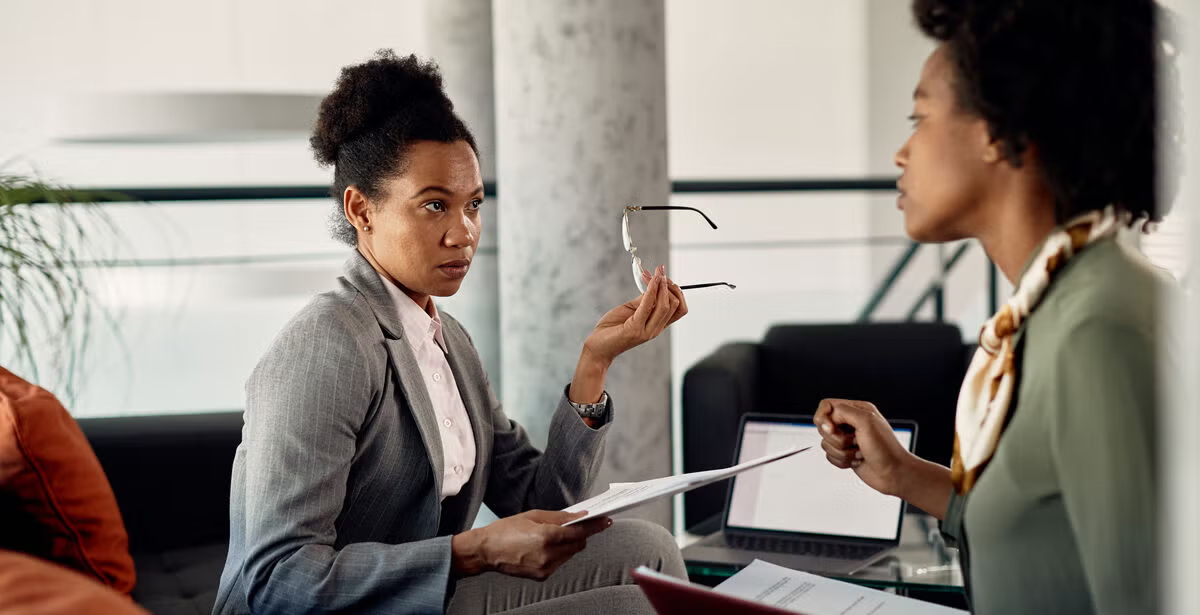 Two professional women review documents in a formal discussion, representing public policy issues and their impact.
