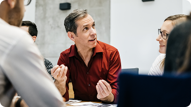 A man speaks to a group of people during a meeting, engaging them with his presentation and discussion.