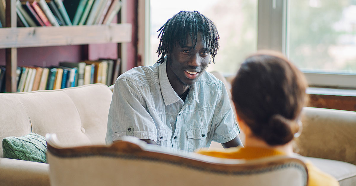 A man sitting on a couch engaged in conversation with a woman.